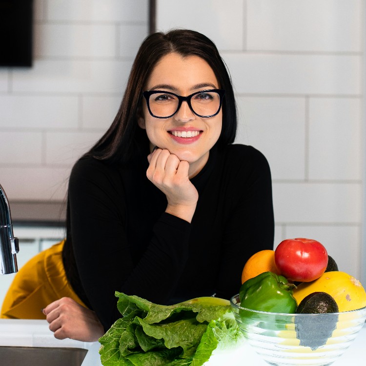 A woman is smiling behind the bowl of vegetables.